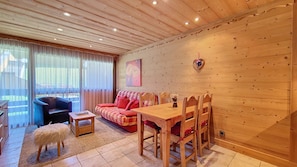 A cozy living room with a wooden ceiling, a sofa, a dining table, and a small dog.