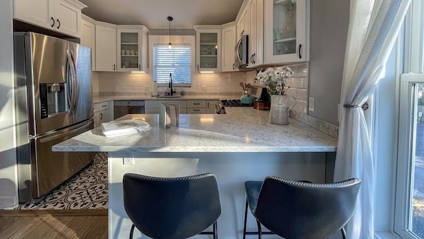 A modern kitchen with white cabinets, stainless steel appliances, and a large island with two black chairs. - Pet Friendly Carriage House Walkable to Beach (West Cape May)