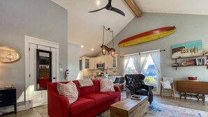 A spacious living room with a red sofa, wooden coffee table, and a ceiling fan. - Pet Friendly Carriage House Walkable to Beach (West Cape May)