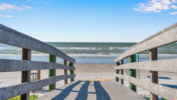 A wooden boardwalk leading to a beach with a clear view of the ocean.