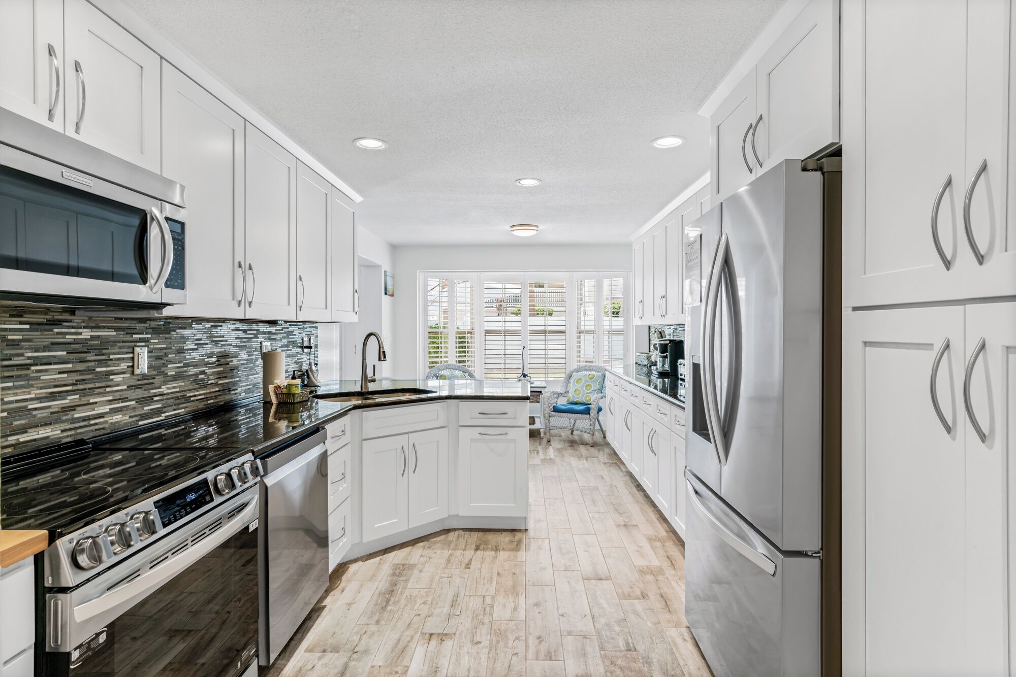 Une cuisine moderne avec des armoires blanches, des appareils en acier inoxydable et un parquet en bois disposé en chevrons.