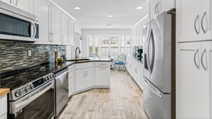 A modern kitchen with white cabinets, stainless steel appliances, and a herringbone wood floor.