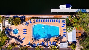 An aerial view of a resort with a large swimming pool, sun loungers, and a dock.