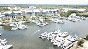 A marina with numerous boats docked, surrounded by a resort with multiple buildings and palm trees.
