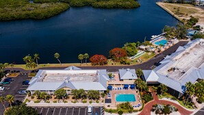 An aerial view of a hotel with a swimming pool, parking lot, and a view of the surrounding water and greenery.