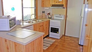 A compact kitchen with wooden cabinets, a microwave, a stove, and a refrigerator. - Home Away in Callala Bay (Callala Bay)