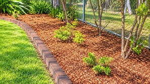 A landscaped garden with a brick border, mulch, and young trees.