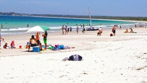 A beach with people walking, a sailboat, and a beach umbrella. - Home Away in Callala Bay (Callala Bay)