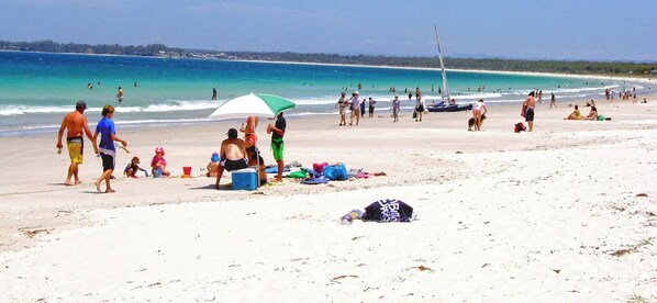 A beach with people walking, a sailboat, and a beach umbrella. - Home Away in Callala Bay (Callala Bay)