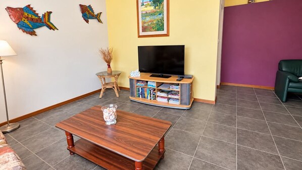 A living room with a wooden coffee table, a television on a stand, a bookshelf, and a painting on the wall.