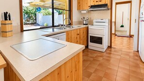 A modern kitchen with a large island, a double oven, and a window with a view of greenery. - Home Away in Callala Bay (Callala Bay)