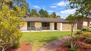 A single-story house with a tiled roof, a covered patio with chairs, and a well-maintained lawn.