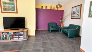 A living room with a TV, books, a sofa, and a vase. - Home Away in Callala Bay (Callala Bay)