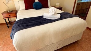 A neatly made bed with a white comforter and a dark blue blanket, a folded towel, and a small bedside table with a lamp. - Home Away in Callala Bay (Callala Bay)