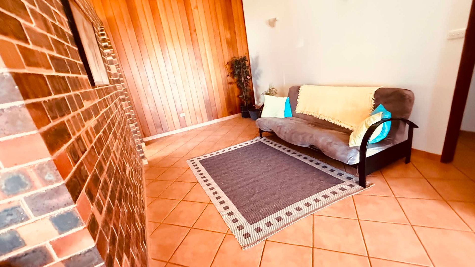A room with a tiled floor, a sofa with cushions, a small rug, and a wooden wall.