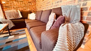 A living room with a dark-colored sofa, a patterned rug, and a brick wall.