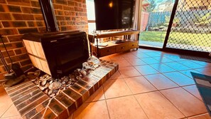 Une cheminée avec un téléviseur posé sur un meuble, un buffet en bois et une vue sur le jardin à travers une porte vitrée.