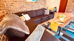 A living room with a dark brown sofa, a coffee table with a yellow cover, and a patterned rug. - The Happy Shack family house (Callala Bay)