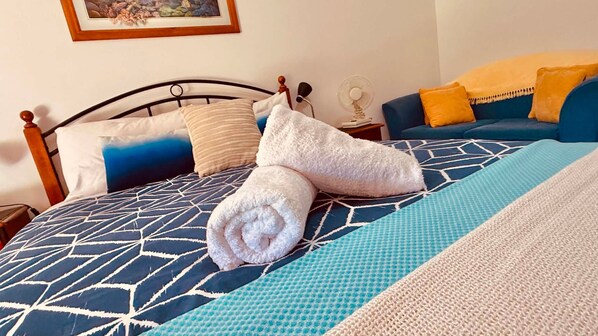 Un lit bien fait, avec une couvre-lit à motifs géométriques, une couverture bleue et blanche, et deux serviettes enroulées.
