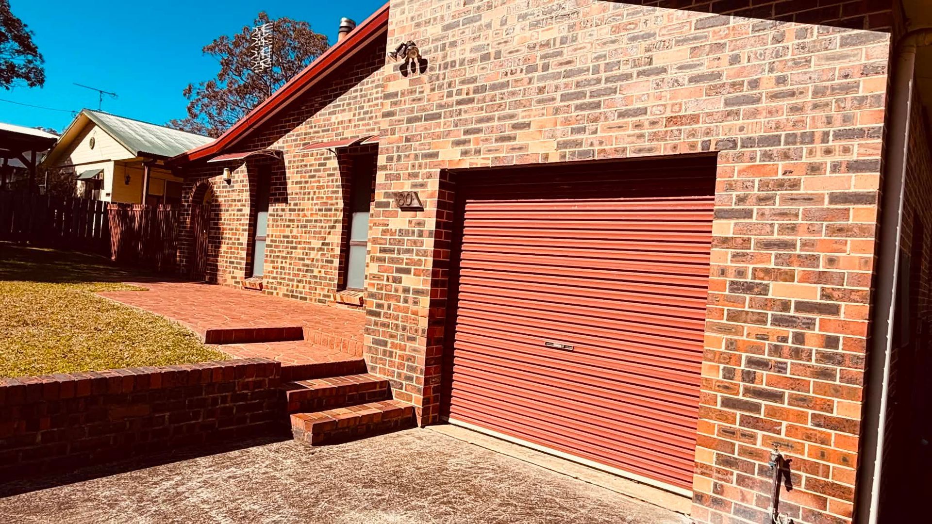 A brick building with a red garage door, a small set of steps leading to the entrance, and a clear sky.