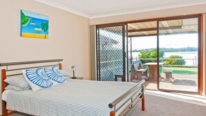 A bedroom with a bed, a nightstand, a painting, and a sliding glass door leading to an outdoor area with a table and chairs.