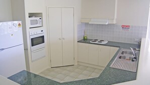 A compact kitchen with a refrigerator, microwave, oven, and a sink with a stainless steel basin.