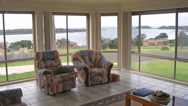 A room with two armchairs facing a large window overlooking a body of water and a distant landscape.