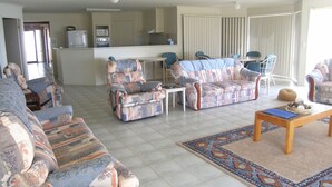 A living room with patterned sofas, a coffee table, and a kitchen area in the background.