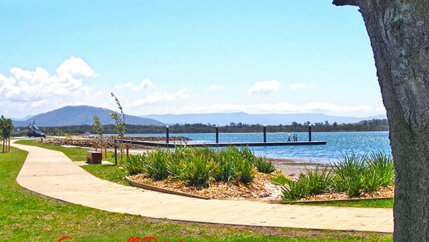 A waterfront park with a concrete path, benches, and a dock.