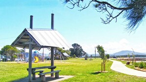 A park with a metal-roofed pavilion, picnic tables, a playground, and a walking path.