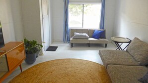 A living room with a sofa, a round rug, a small table, a TV stand, and a plant.