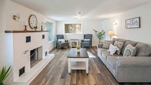 Ein Wohnzimmer mit Kamin, zwei Sesseln, einem Sofa, einem Couchtisch und einer Wanduhr.