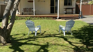 Two white plastic chairs on a lawn in front of a building with a covered patio area. - My Hideaway - Pet Friendly (Callala Beach)