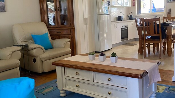 A living room with a beige armchair, a coffee table with three potted plants, and a wooden cabinet. - My Hideaway - Pet Friendly (Callala Beach)