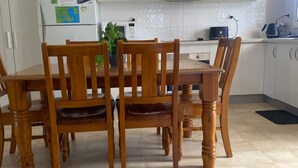 A dining area with a wooden table and chairs, a refrigerator, a microwave, and a kettle on the counter. - My Hideaway - Pet Friendly (Callala Beach)