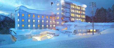 Un hotel de varios pisos con ventanas iluminadas y fachada cubierta de nieve.