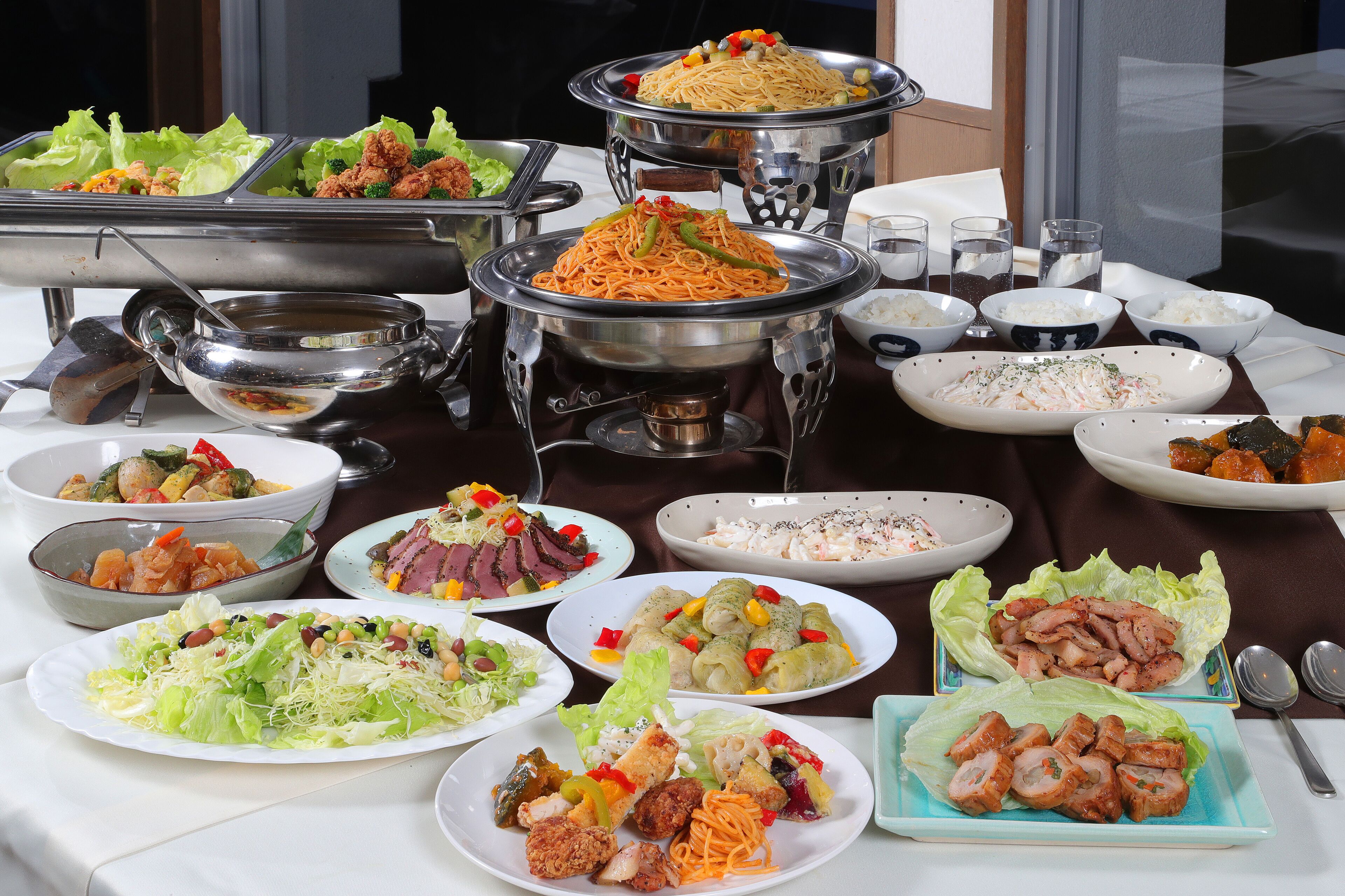 Une table de buffet proposant divers plats, notamment des salades, de la viande et des nouilles.