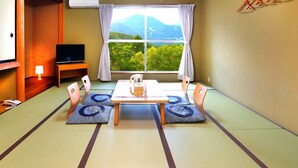 A traditional Japanese room with tatami flooring, a low table with cushions, a television, and a view of mountains through a large window. - Ryuo Mountain Hotel (Yamanouchi)