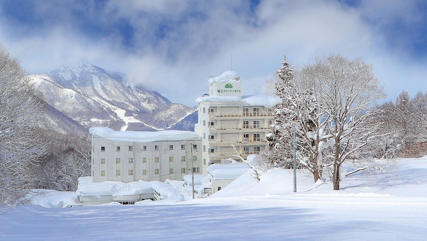 A snow-covered building with a mountain backdrop, surrounded by trees and snow. - Ryuo Mountain Hotel (Yamanouchi)