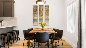 A dining area with a wooden table, black chairs, and a potted plant. There are three vertical paintings on the wall above the table. - St. George Getaway, Brand New 5 BD Luxury Townhome (St. George)