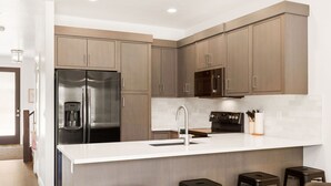 A modern kitchen with a stainless steel refrigerator, a built-in coffee maker, and a microwave. There are four stools and a bar counter. - St. George Getaway, Brand New 5 BD Luxury Townhome (St. George)