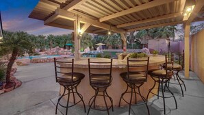 An outdoor bar area with a pool, surrounded by palm trees and a wooden pergola. - Pickle+Basketball|Billiards|9bdr+6bath|Saltwater (Desert Hot Springs)