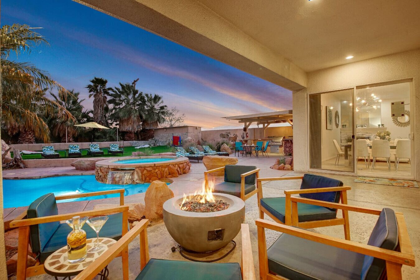 Un espacio de piscina con sillones, una fogata y un comedor con sillas y mesa.