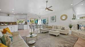 A spacious living area with a white sofa, a coffee table, and a fireplace. There is a dining area with chairs and a kitchen in the background. - Pickle+Basketball|Billiards|9bdr+6bath|Saltwater (Desert Hot Springs)