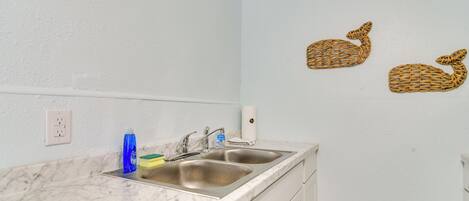 A kitchen with two stainless steel sinks, a marble countertop, and a white wall with two woven wall art pieces.