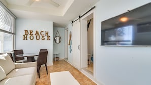 Un salón decorado con motivos playeros, con un sofá, sillas, una mesa y un televisor de pared.