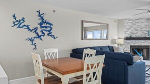 Un salon comprenant une table à manger, des chaises blanches, un canapé bleu, une cheminée et un miroir fixé au mur.
