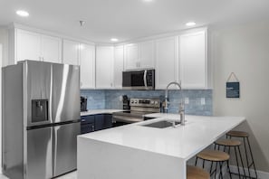 A modern kitchen with white cabinets, stainless steel appliances, a central island with stools, and a blue backsplash.