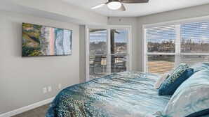 Une chambre à coucher avec un lit, un ventilateur de plafond, un tableau et une vue par la fenêtre.