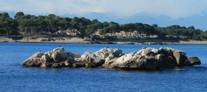 A rocky outcrop in a body of water with a forested hill in the background. - Apartaments l'Escala Centre  2 (Escala, L')